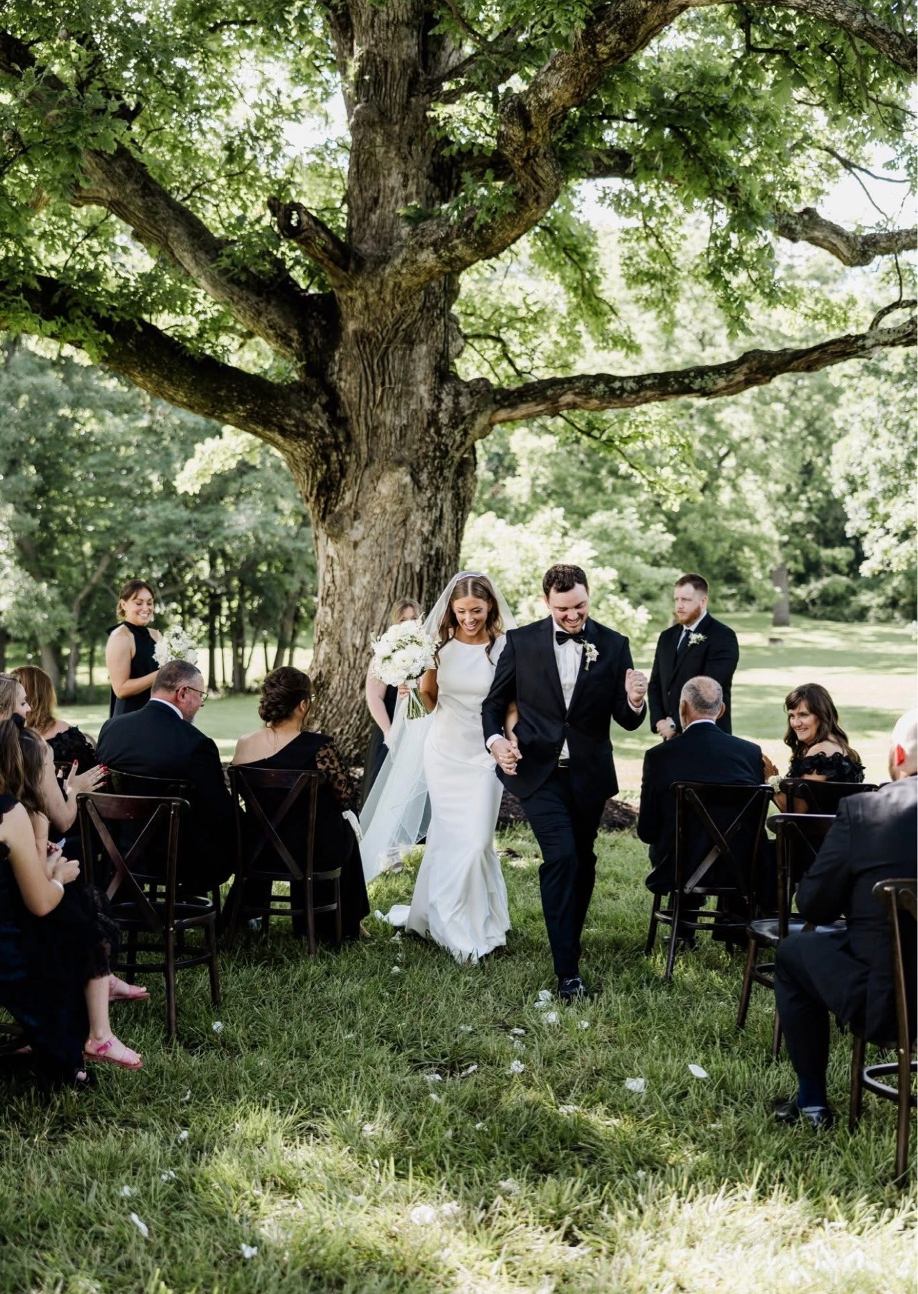 The bride and groom walk back up the aisle under the oak tree as guests cheer