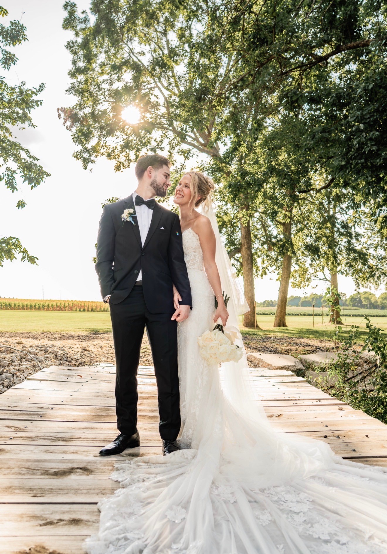 The bride and groom standing together on a wooden boardwalk under the trees