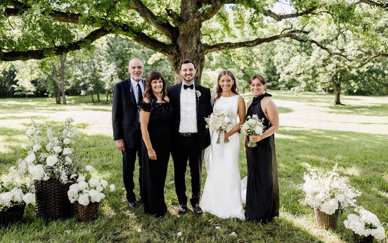 The bride and groom with her family under an oak tree, white flower arrangements at their feet