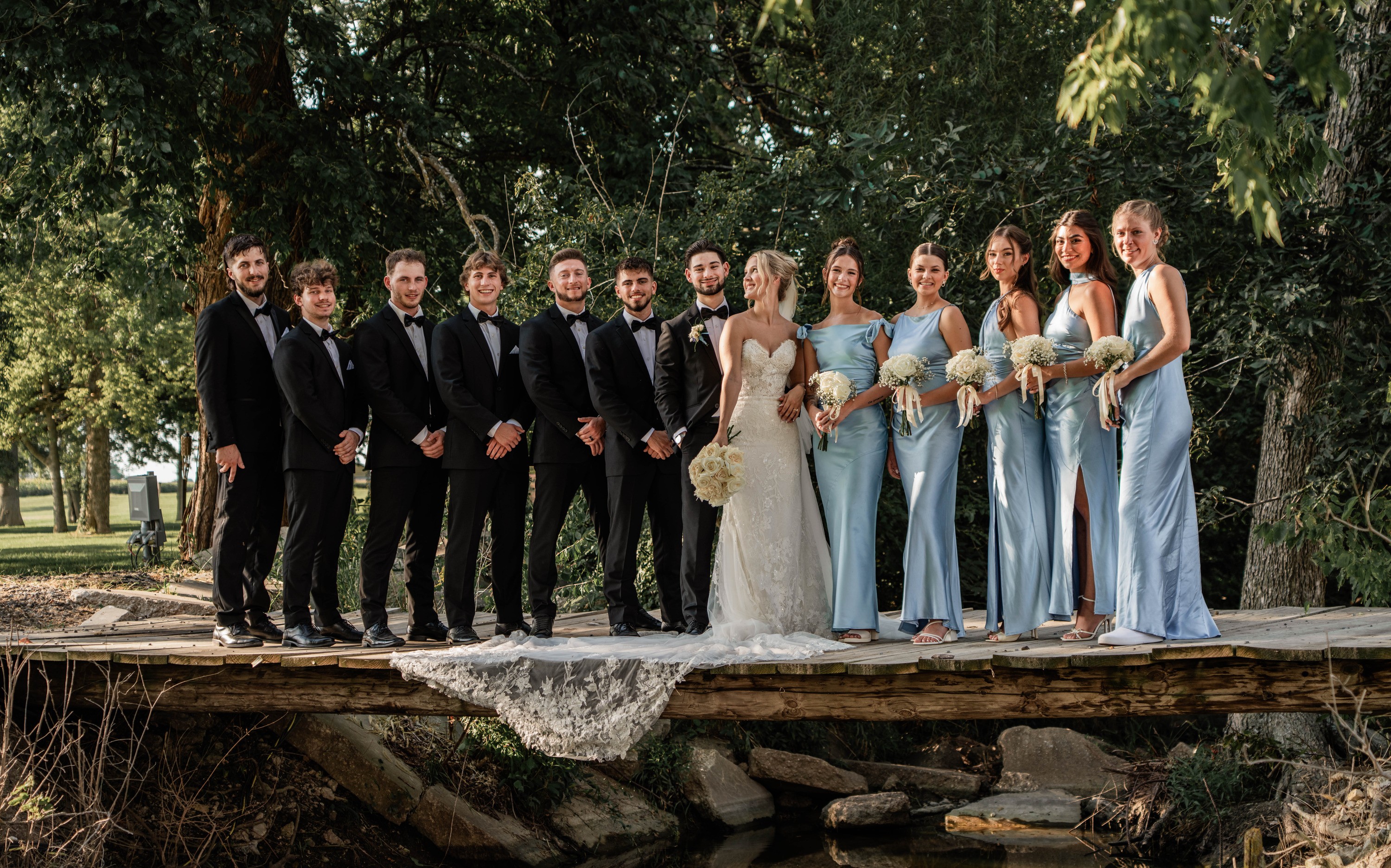 The bridal party lined up on a wooden bridge, bridesmaids in pale blue satin